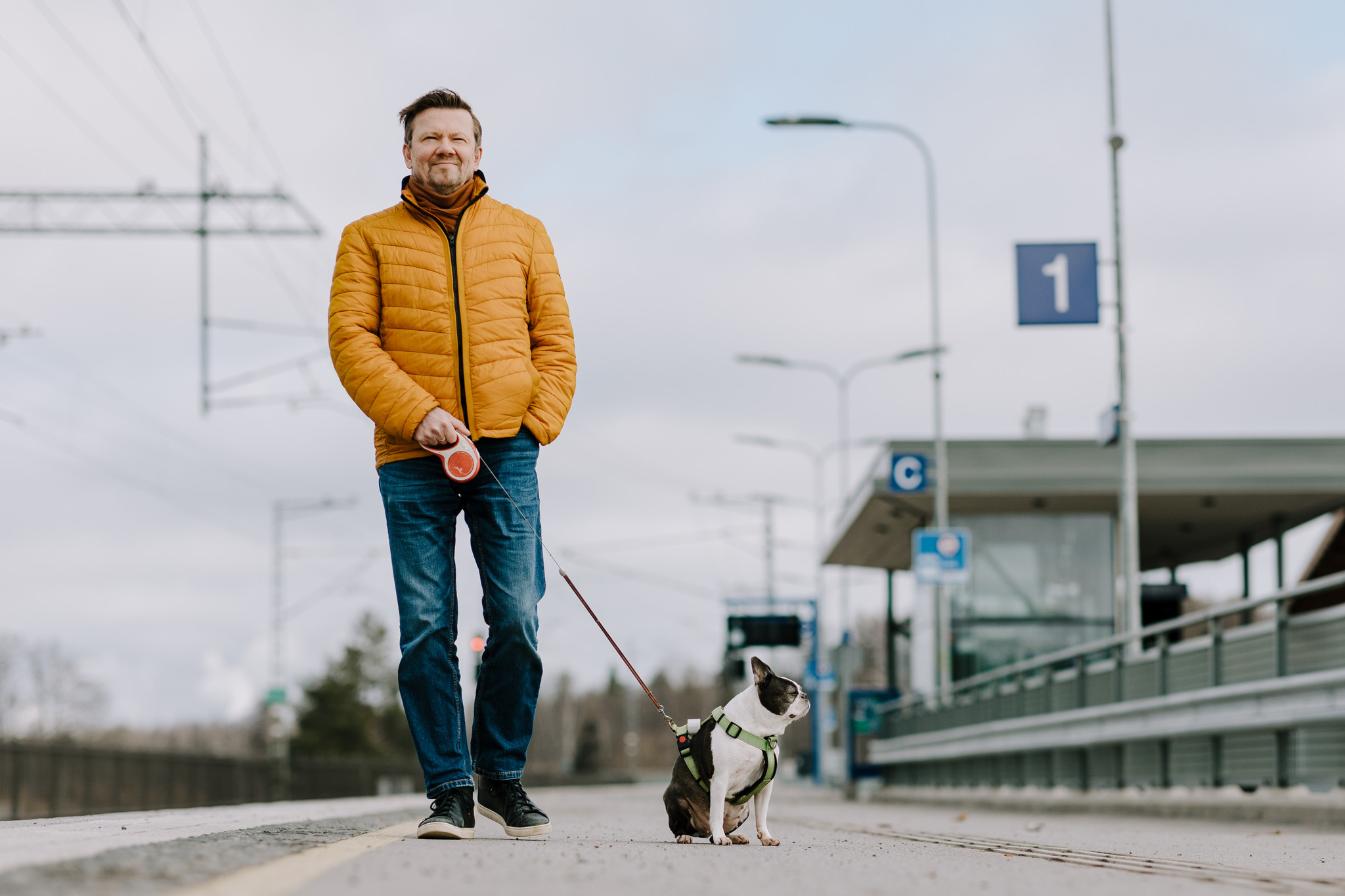 Teatterinjohtaja Timo Rissanen kävelee Imatran juna-asemalla hymyillen ja taluttaen mustavalkoista pientä koiraa.