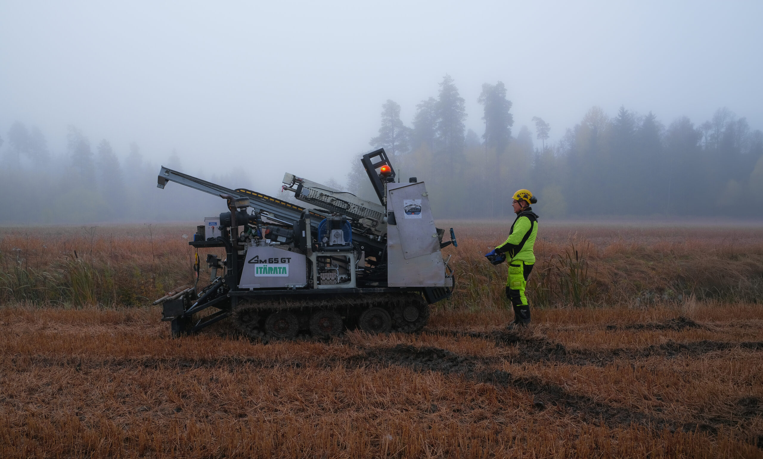 Työkone ja työmies pellolla kairausvaunun kanssa.